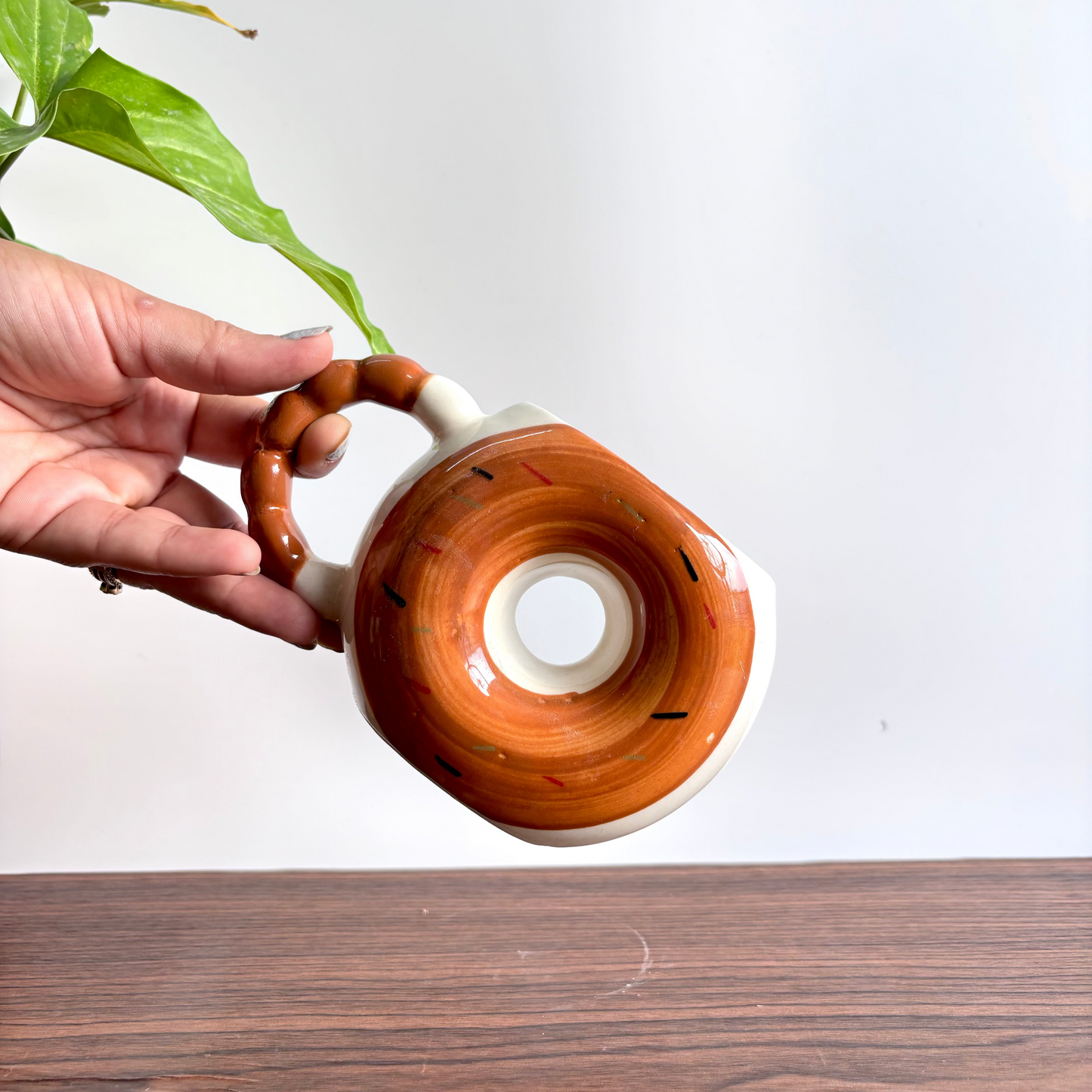 Hand holding a ceramic teapot with a wooden handle on a white background