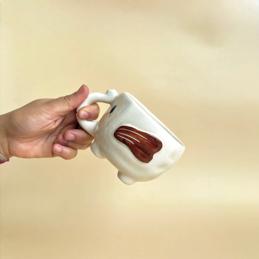 Hand holding a white mug with a brown handle against a beige background