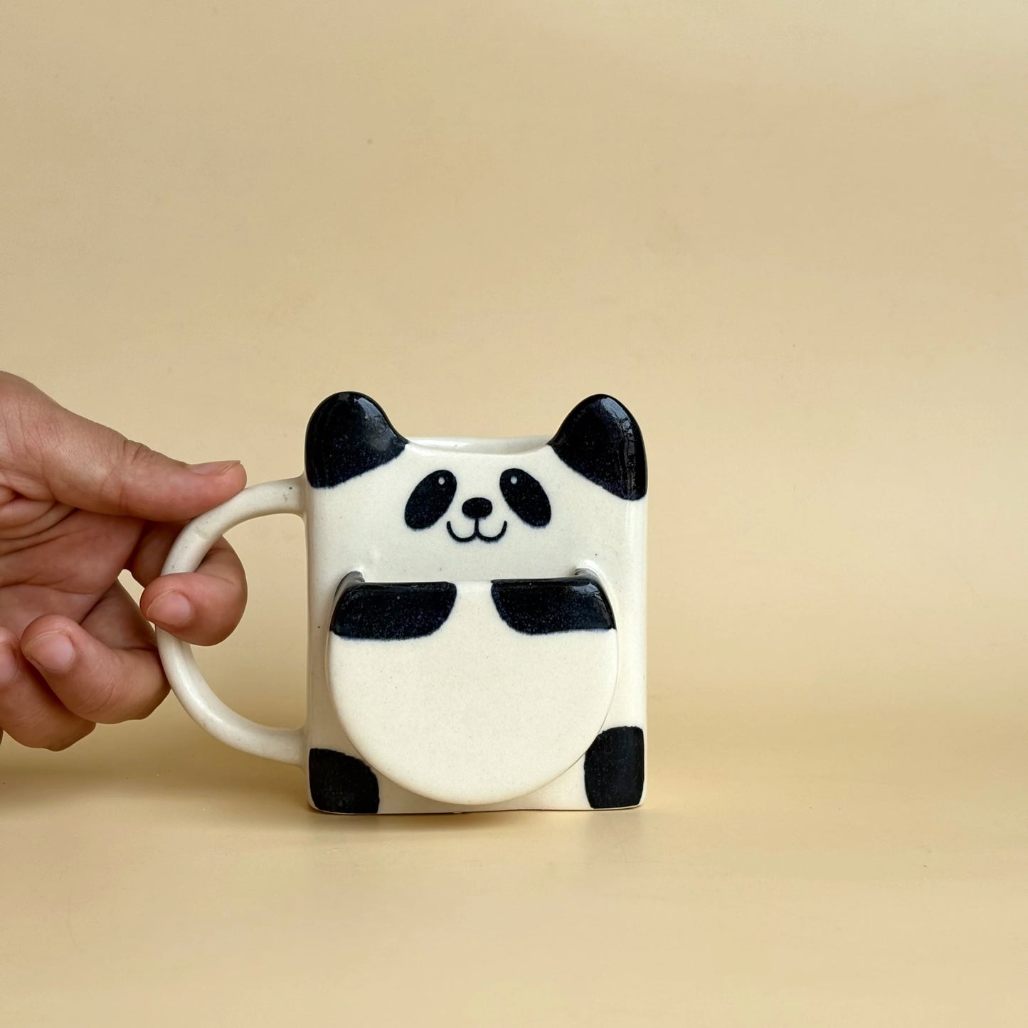 Panda mug held by a hand against a beige background