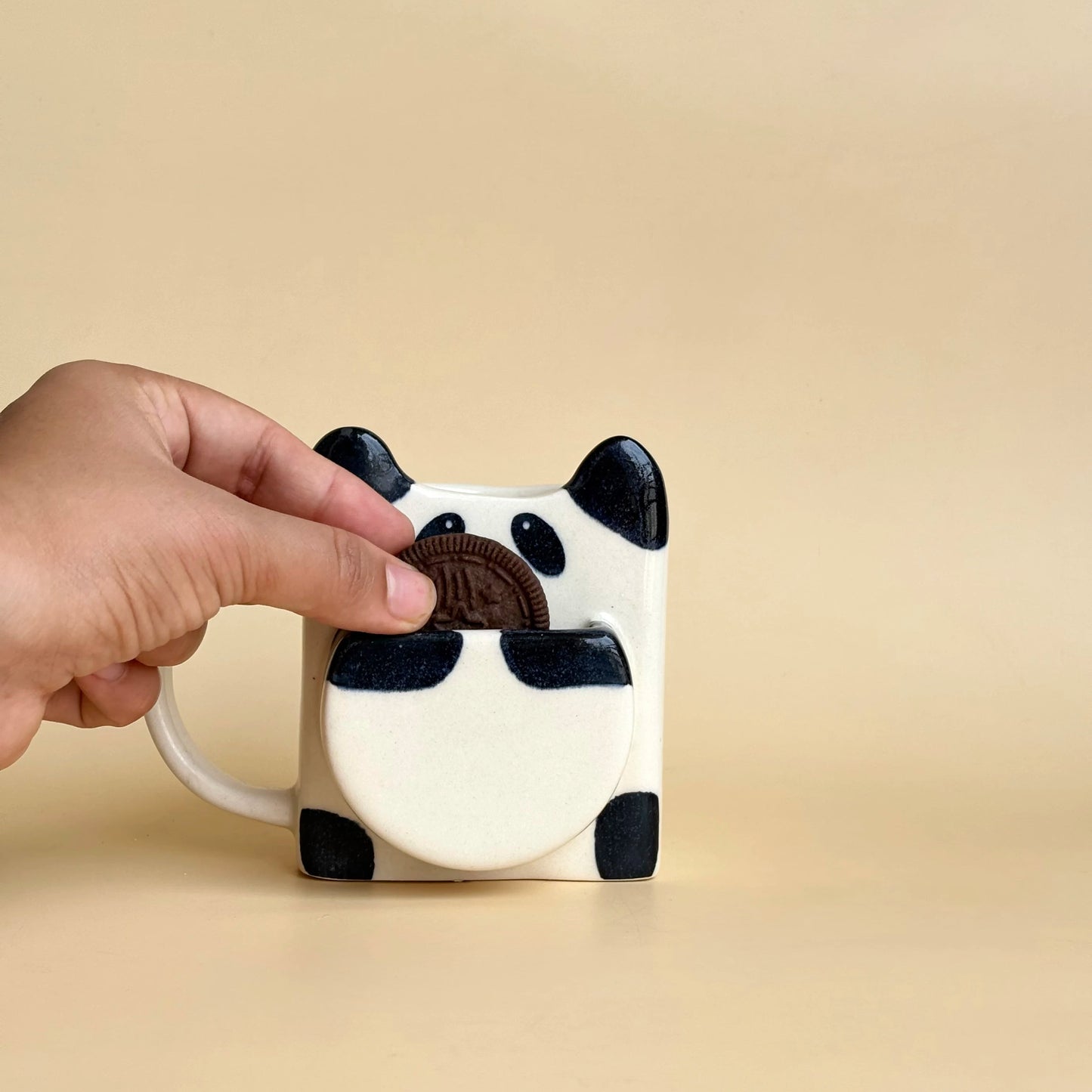 Hand holding a panda mug against a beige background