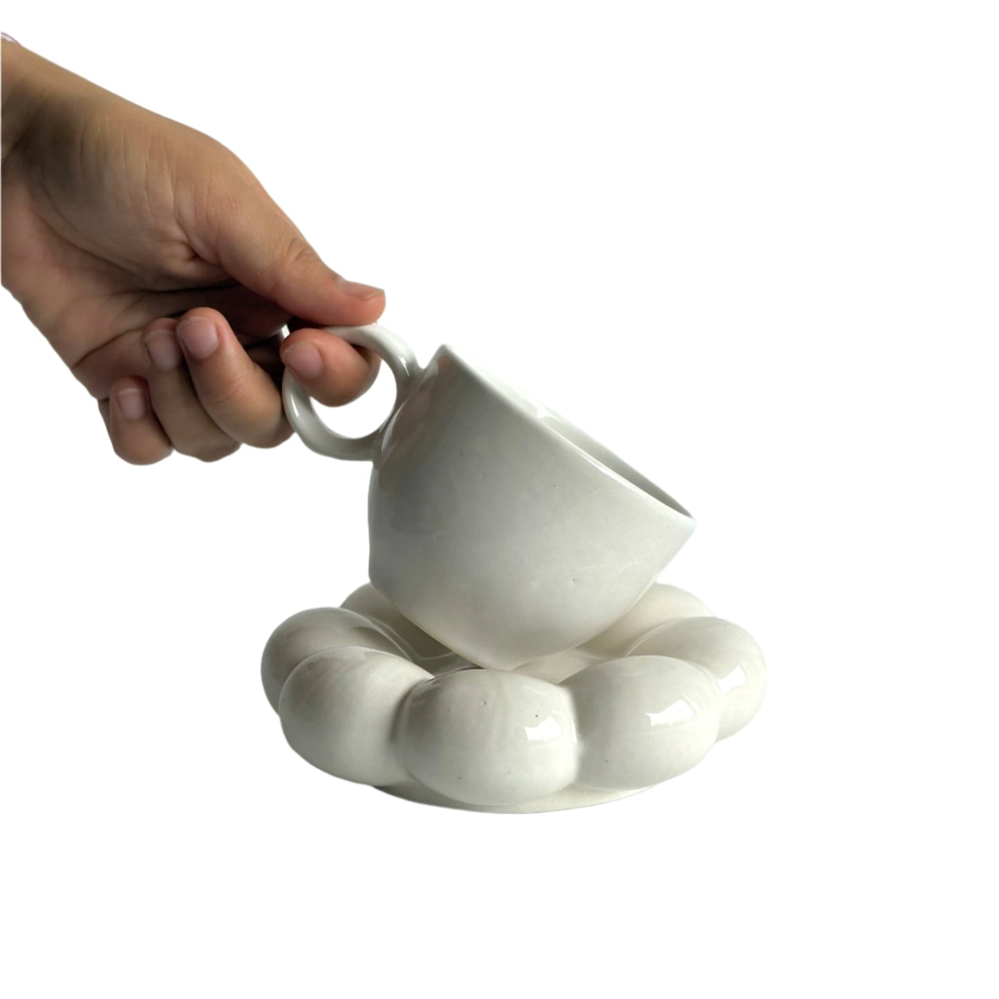 White ceramic cup and saucer held by a hand on a light gray background