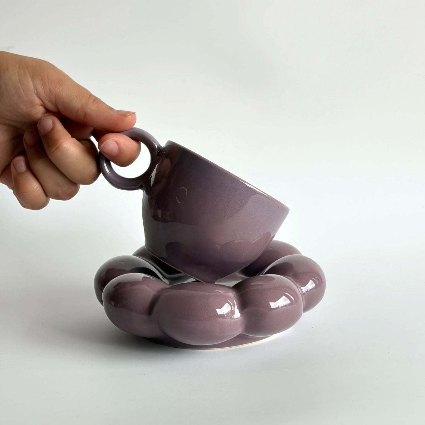 Purple ceramic cup and saucer held by a hand on a white background