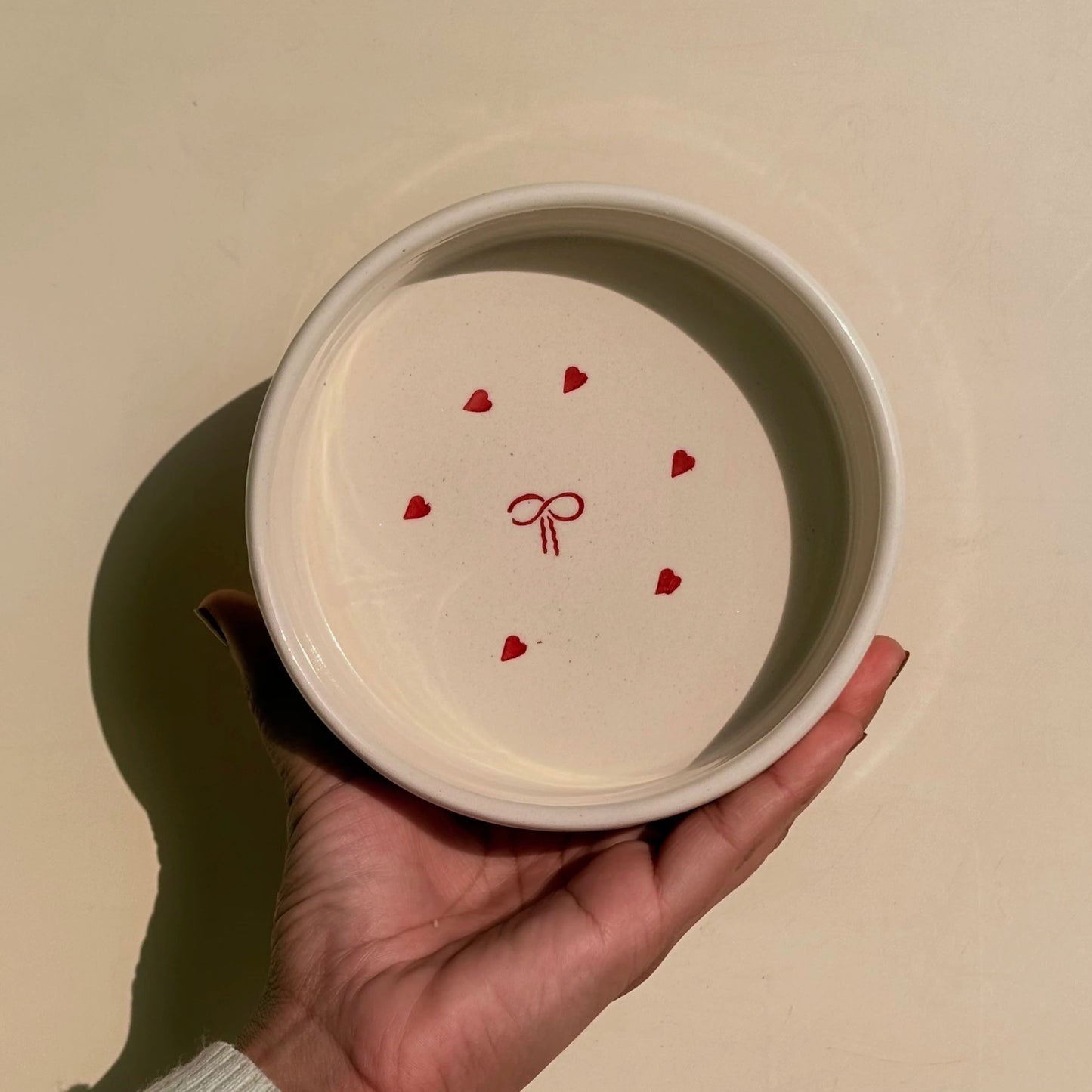Hand holding a white ceramic bowl with red heart and bow design