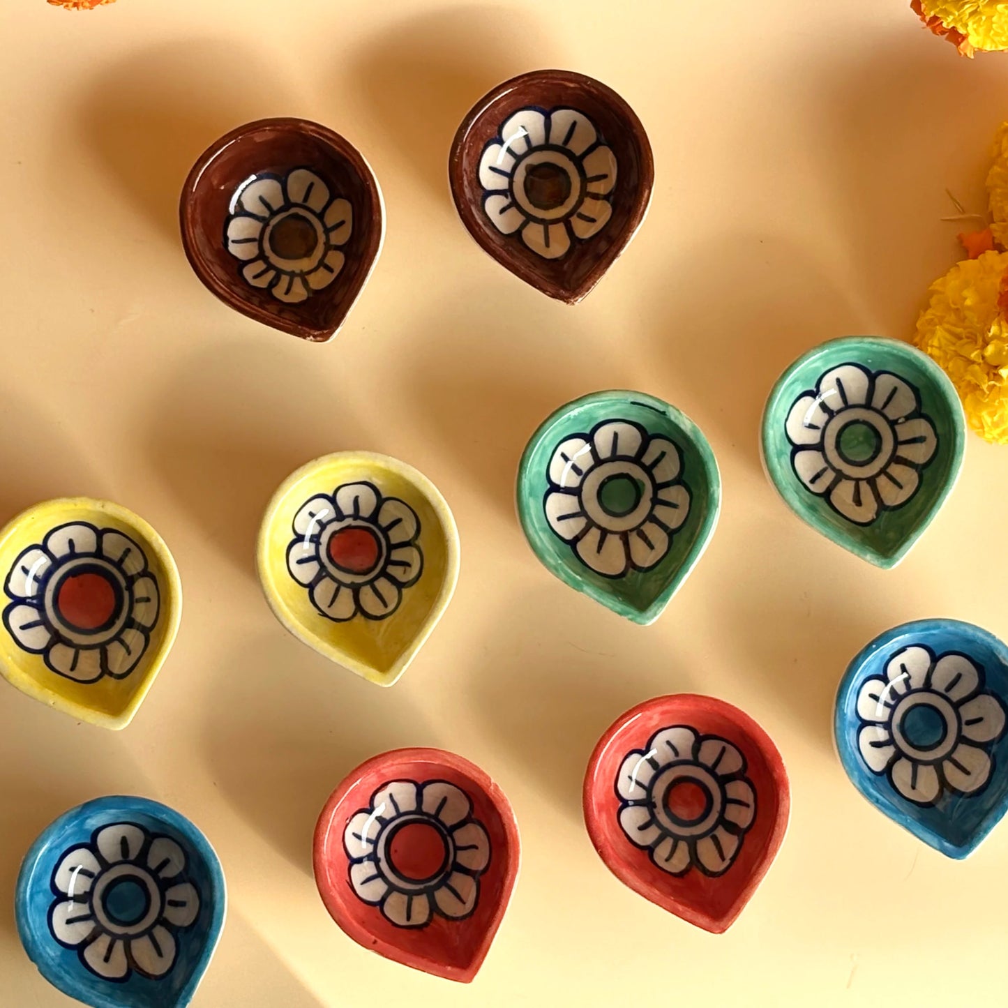 Colorful flower-shaped chocolates on a beige surface with flowers around.