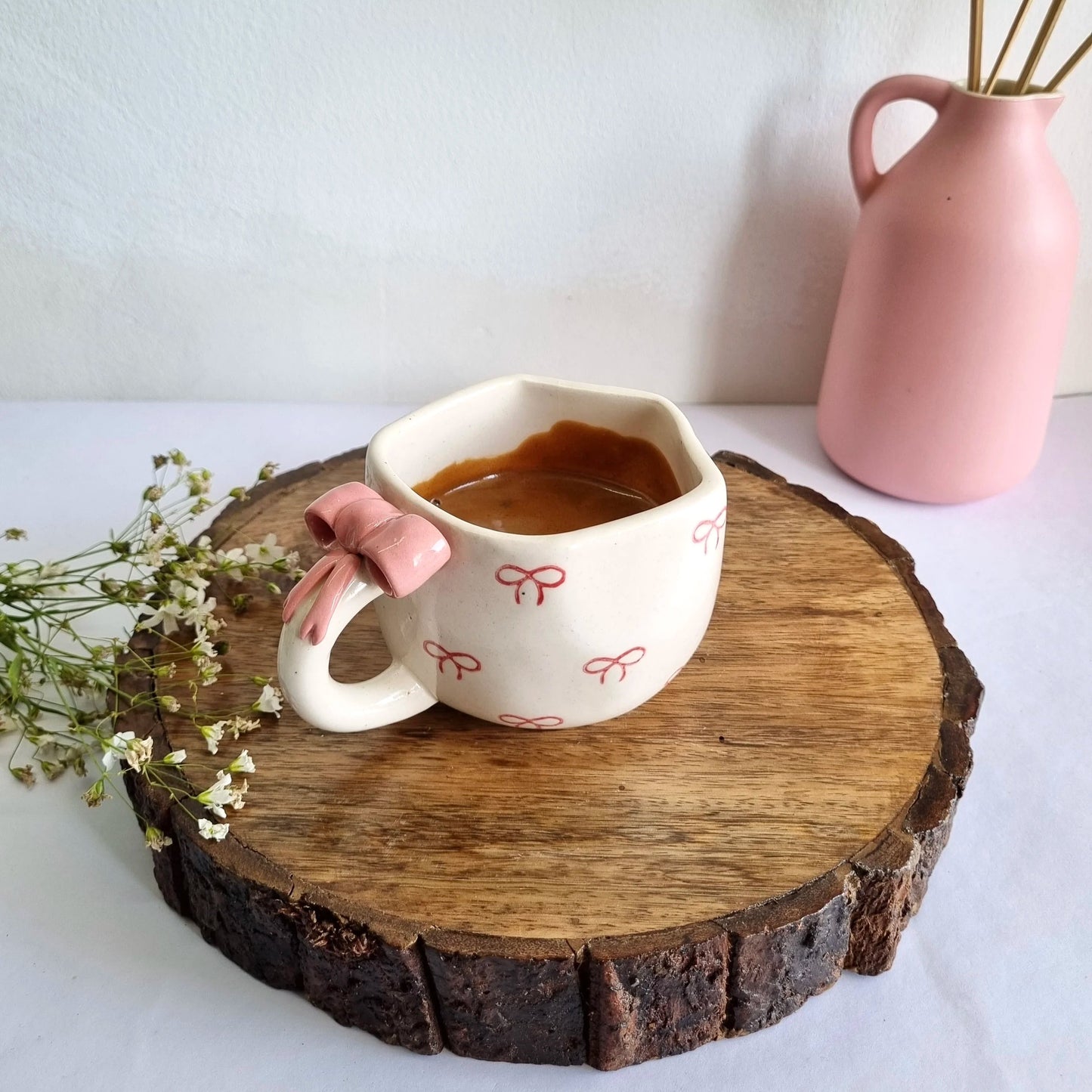 Cup of coffee on a wooden coaster with a pink vase in the background