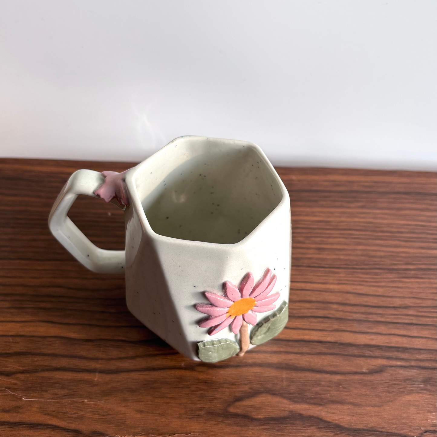 Ceramic mug with a pink flower design on a wooden surface