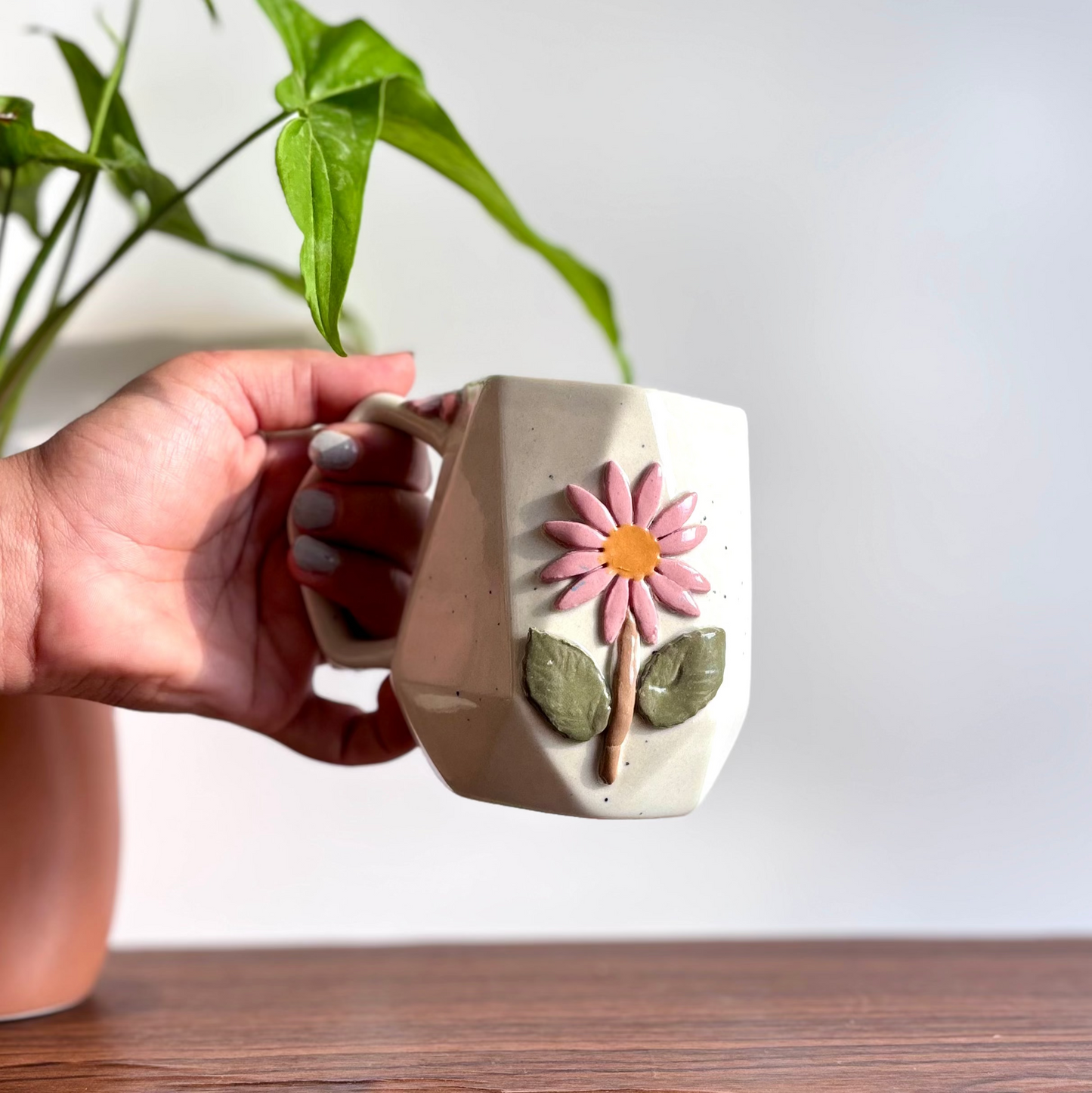 Hand holding a ceramic mug with a floral design on a wooden surface.