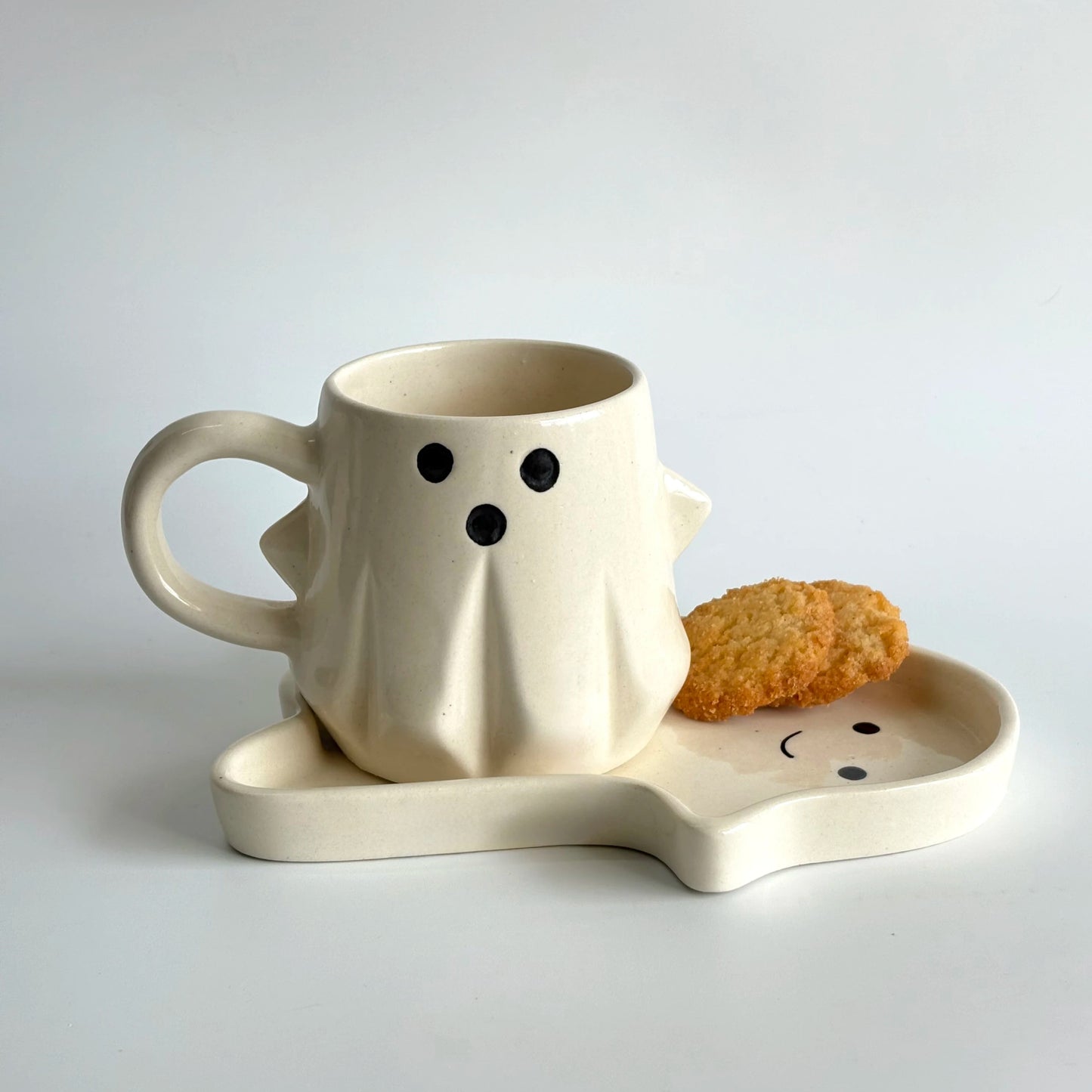 Ceramic ghost-shaped mug with matching saucer on a light gray background