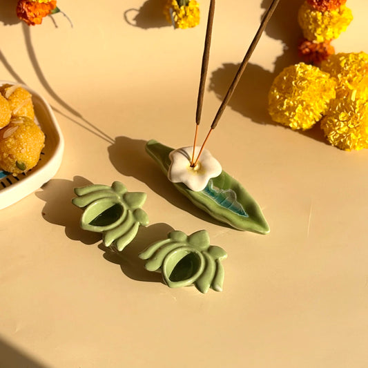 Ceramic incense holder shaped like a leaf with incense sticks on a beige surface with decorative flowers.
