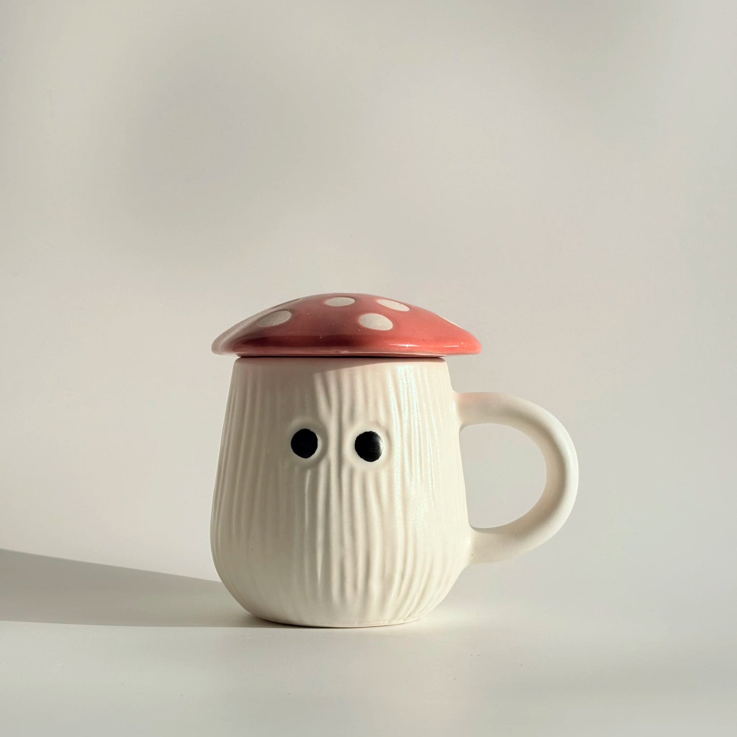 White ceramic mug with a red lid resembling a mushroom on a light gray background