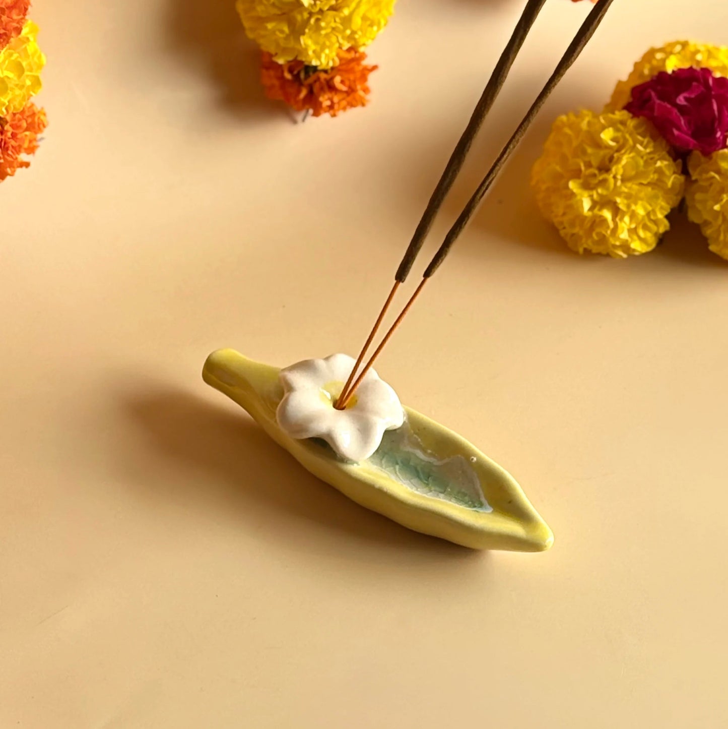Incense sticks on a leaf-shaped holder with flowers in the background
