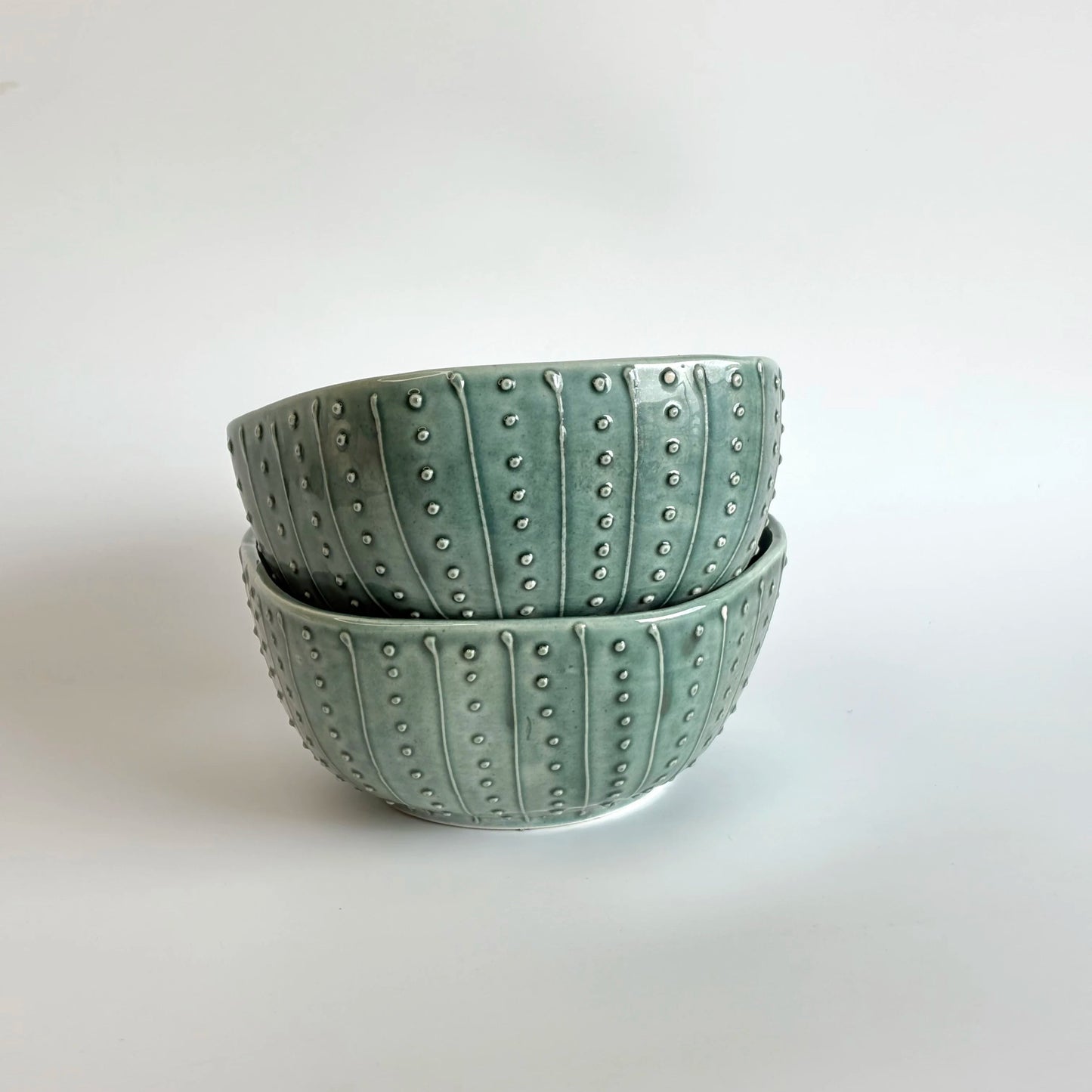 Two green ceramic bowls with textured surface on a white background
