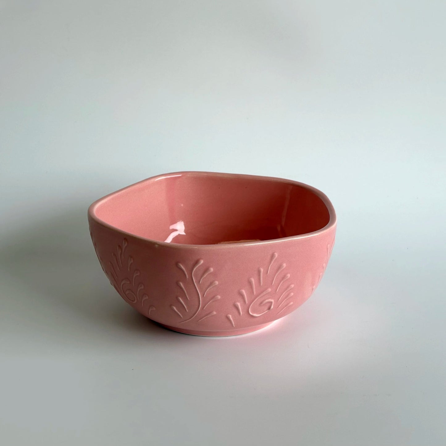 Pink ceramic bowl with floral patterns on a light gray background
