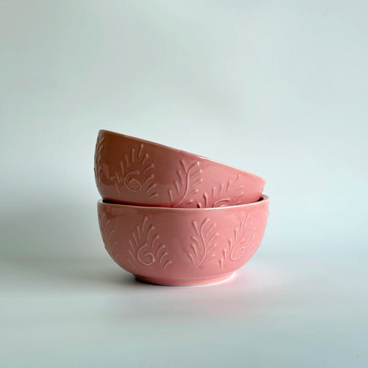 Two pink ceramic bowls with leaf patterns on a light gray background