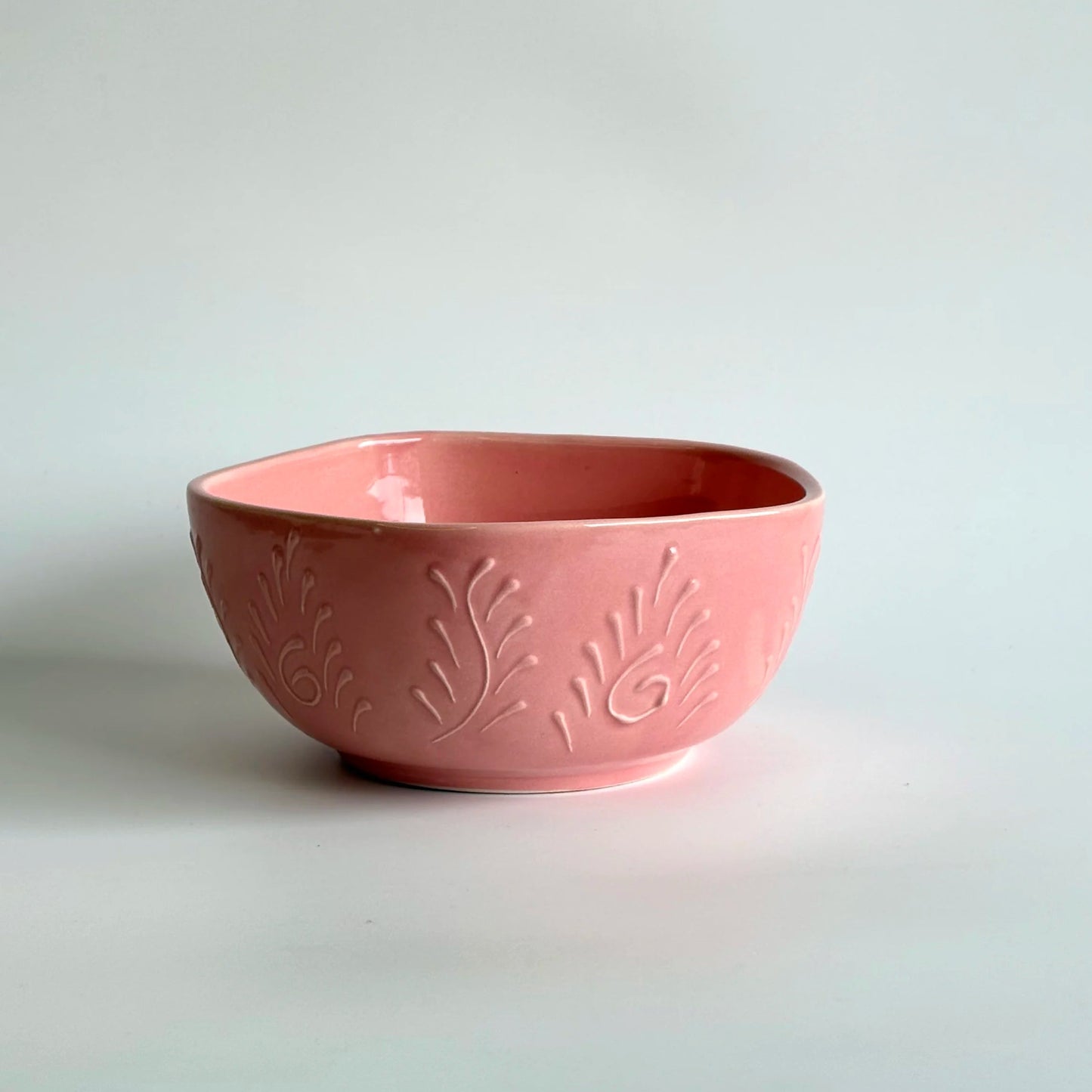 Pink ceramic bowl with embossed design on a light gray background