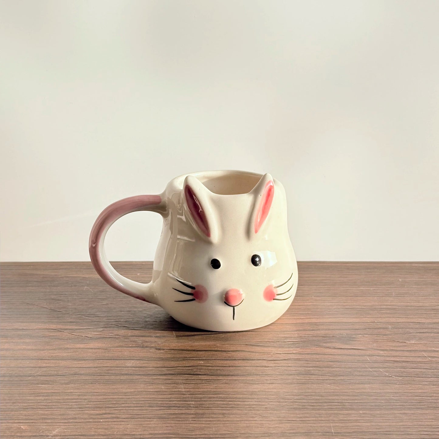 Ceramic mug shaped like a rabbit on a wooden surface with a plain background