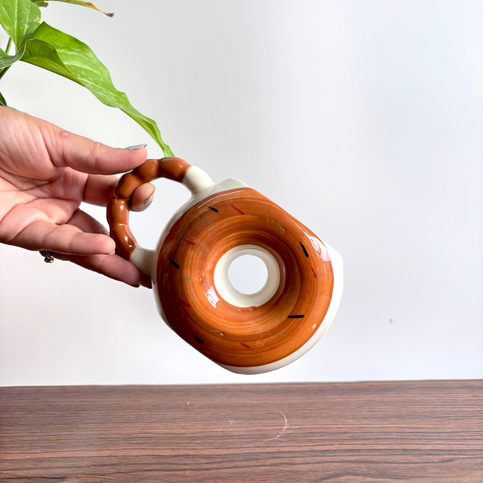 Hand holding a ceramic teapot with a wooden handle on a white background