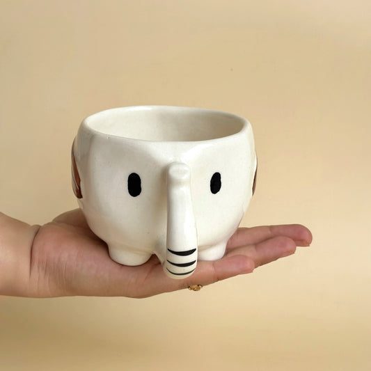 Person holding a white ceramic mug with a cartoonish design on a beige background