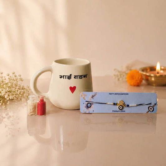 A packaged beaded bracelet with a central gold-toned charm is displayed on a light blue box in front of a white ceramic mug printed with Devanagari text and a small red heart. The scene is styled with dried flowers, small red and pink candles, and a lit diya against a warm beige background with soft shadow overlays.