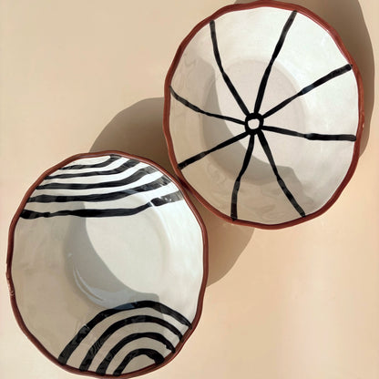 Two ceramic bowls with black line patterns on a beige background