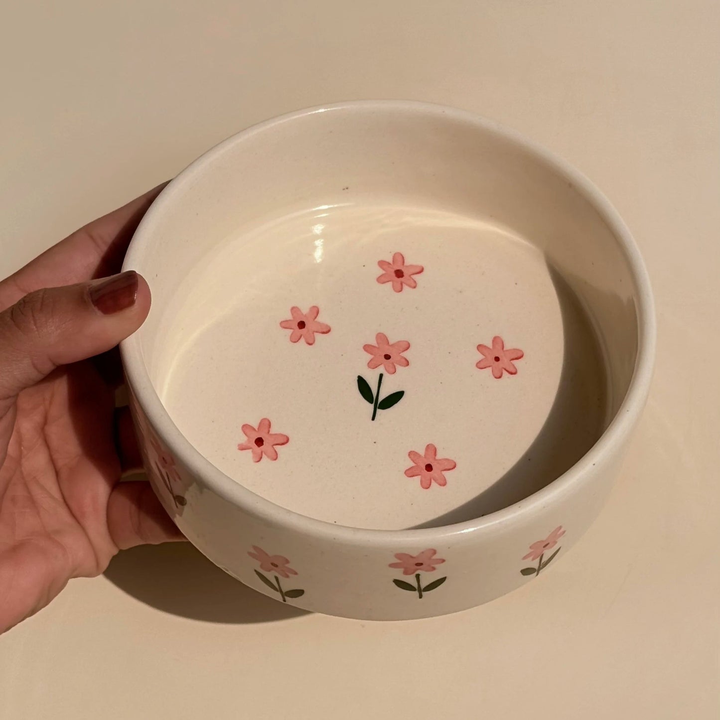 White ceramic bowl with pink floral designs held by a hand on a light background