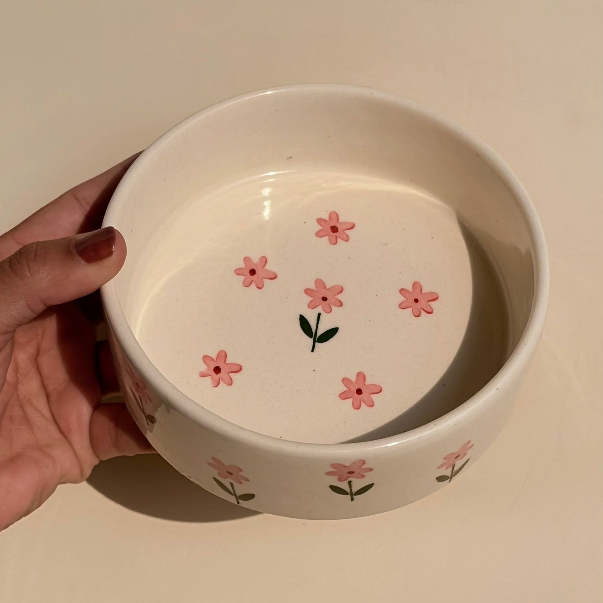White ceramic bowl with pink floral designs held by a hand on a light background