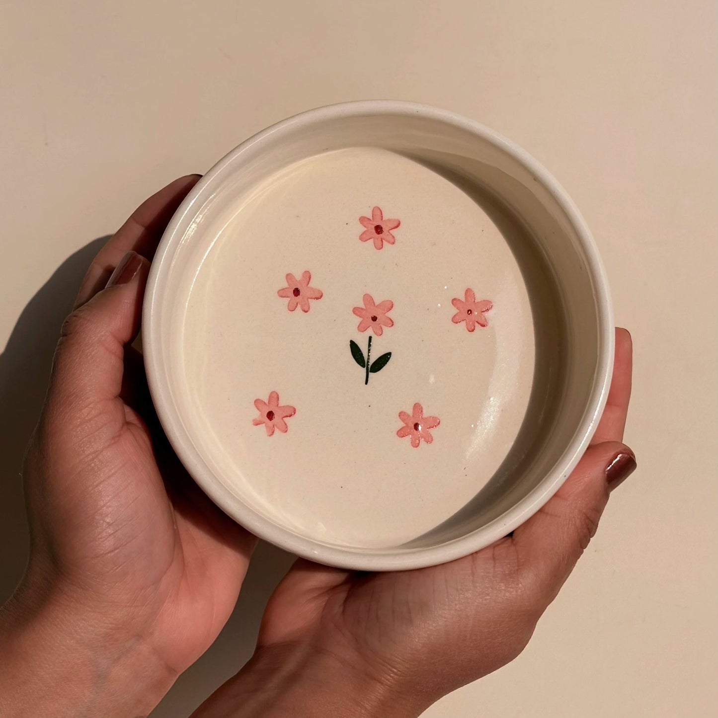 Person holding ceramic bowl with floral design on a beige background