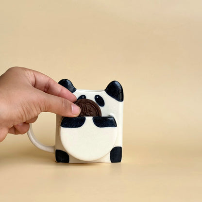 Hand holding a panda mug against a beige background