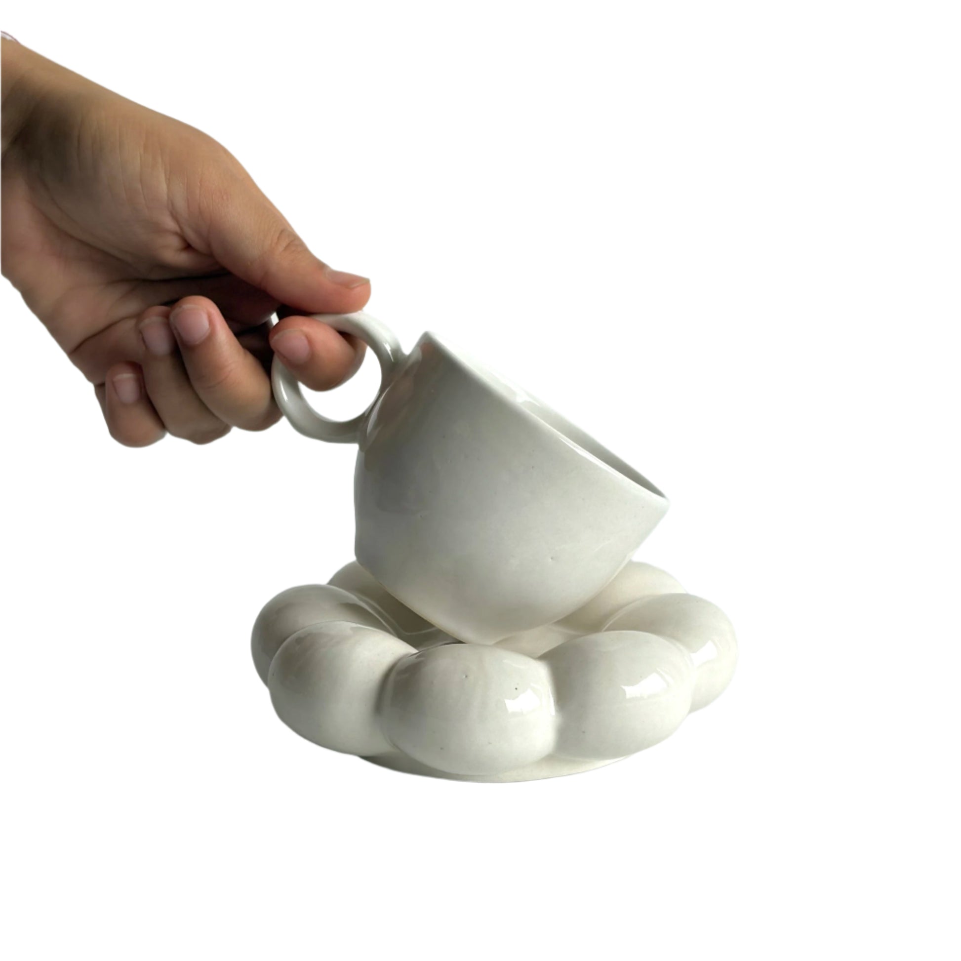 White ceramic cup and saucer held by a hand on a light gray background