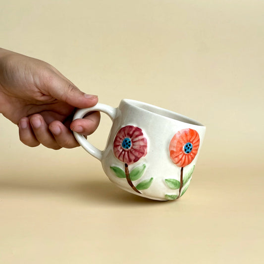 Ceramic mug with floral design held by a hand against a beige background