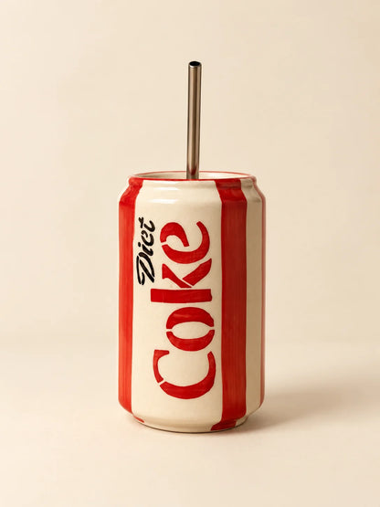A ceramic tumbler designed to look like a Diet Coke can, featuring red and white vertical stripes and the black 'Diet Coke' logo, with a stainless steel straw inserted at the top, set against a solid beige background.