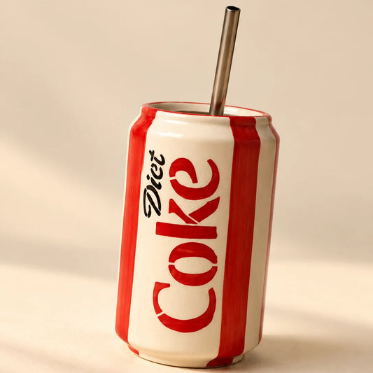 A ceramic mug shaped like a Diet Coke can, featuring red and white vertical stripes and a stainless steel straw, set against a warm beige background.