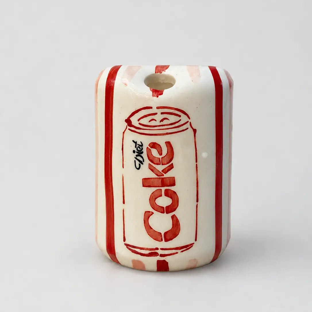 A small cylindrical ceramic charm or bead featuring a retro red and white Diet-Cola can design on an off-white base, with a hole at the top.