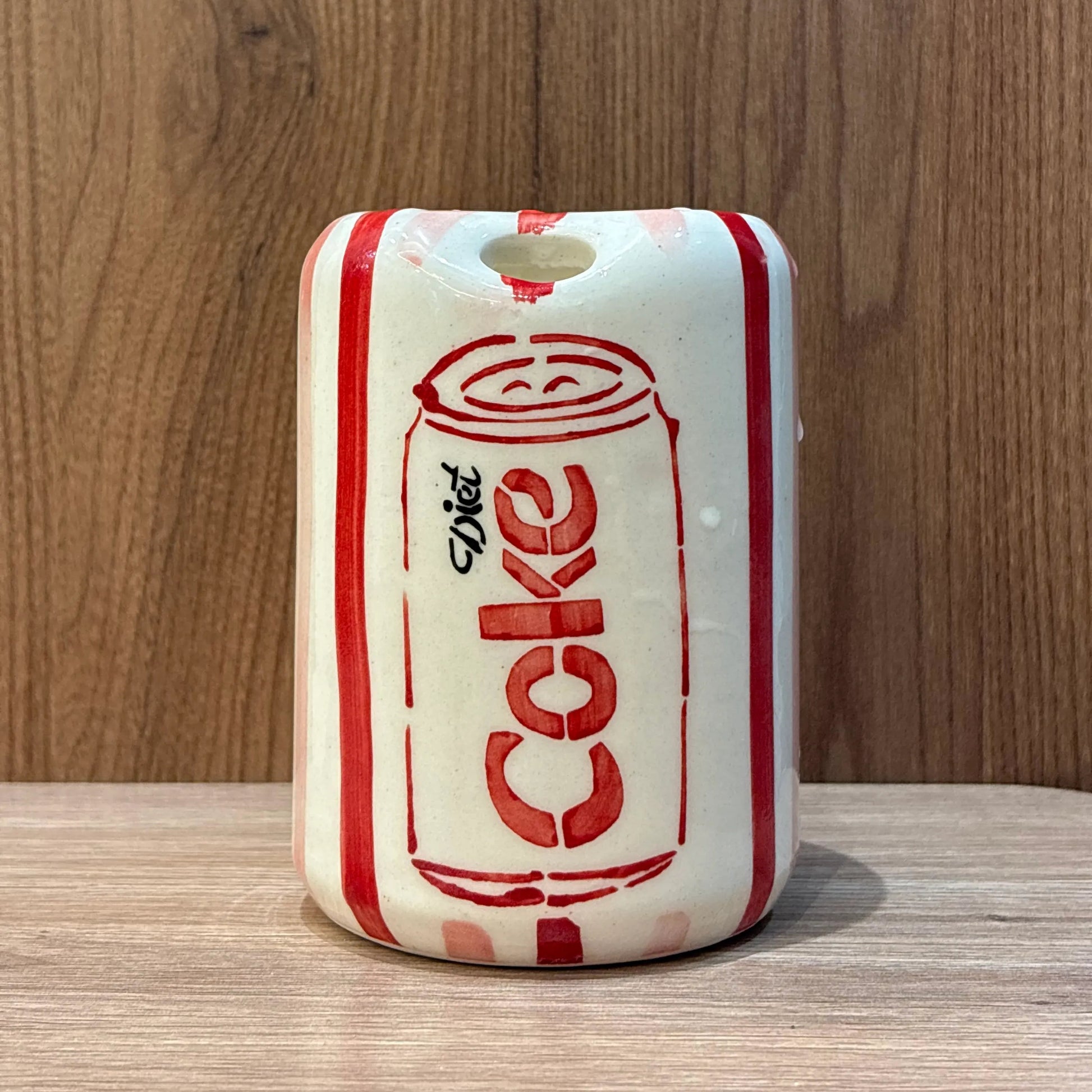 A ceramic mug designed to look like a vintage red and white Diet-Cola can, featuring a small hole at the top for hanging, set against a wooden background.