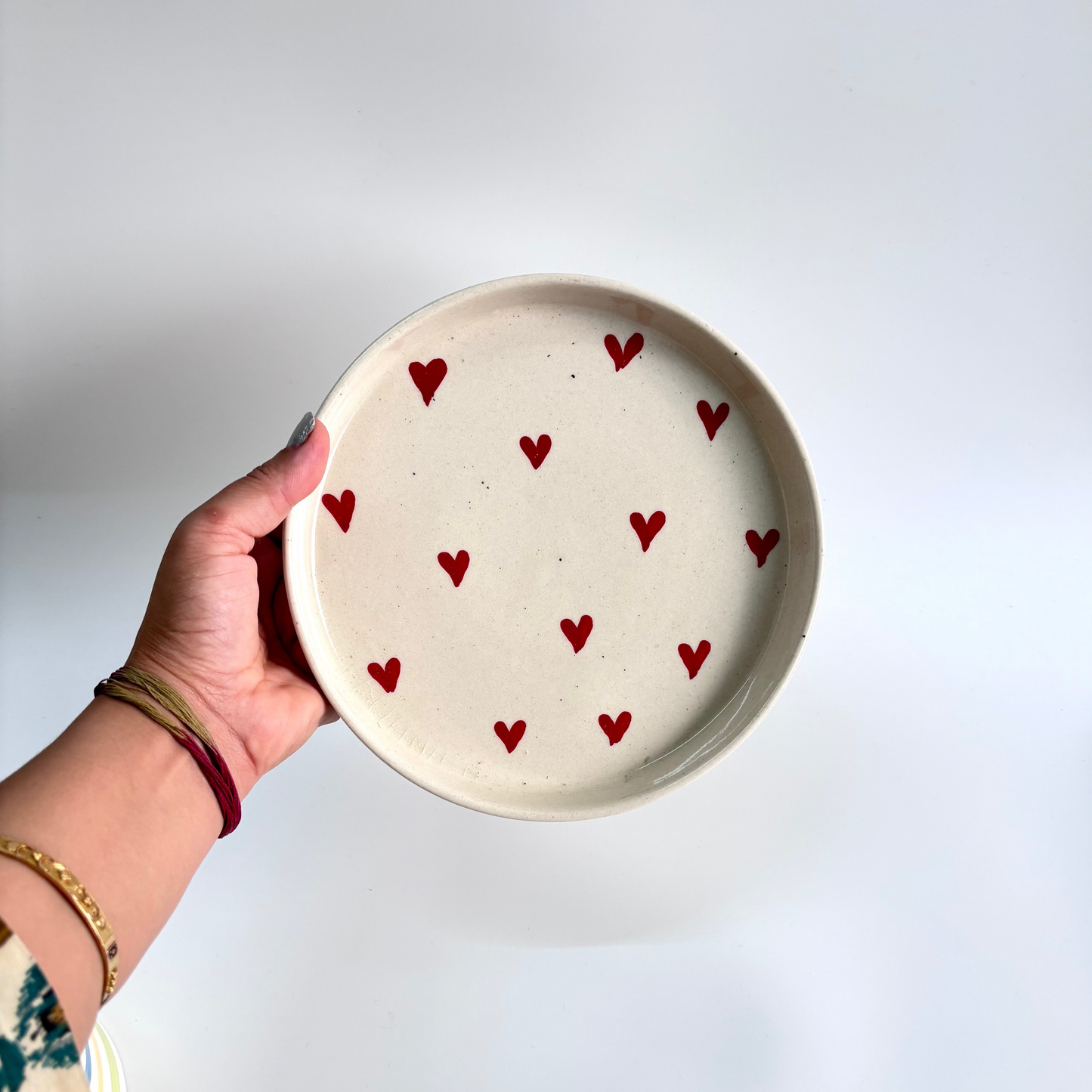 Hand holding a ceramic plate with red heart patterns on a white background