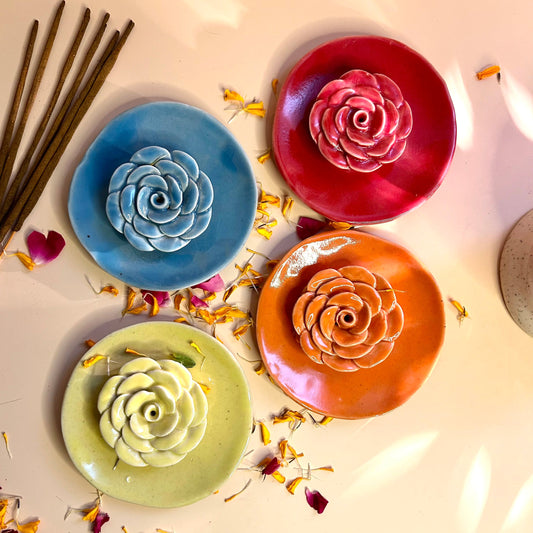 Four ceramic plates with rose designs in blue, red, orange, and green on a light background.