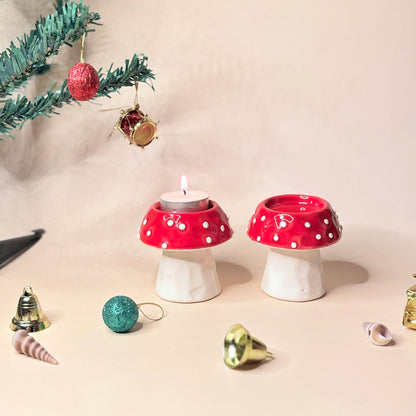 Two red and white polka dot mushroom-shaped candle holders with Christmas decorations on a beige background.