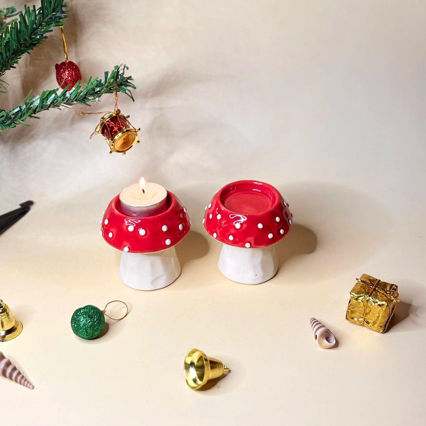 Two red and white polka dot mushroom-shaped candle holders with a lit candle on a light background.