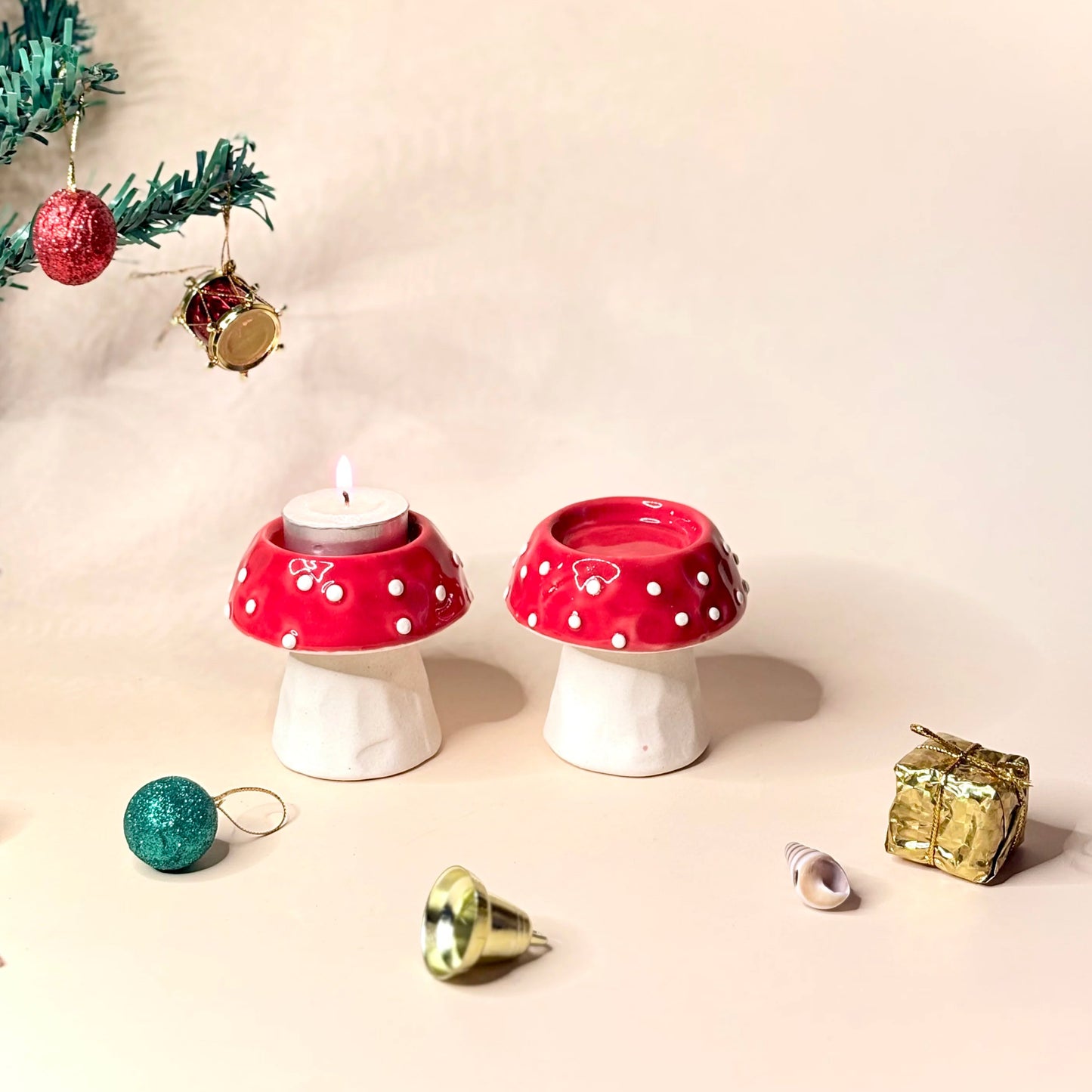 Two red and white polka dot mushroom-shaped candle holders with Christmas decorations on a beige background.