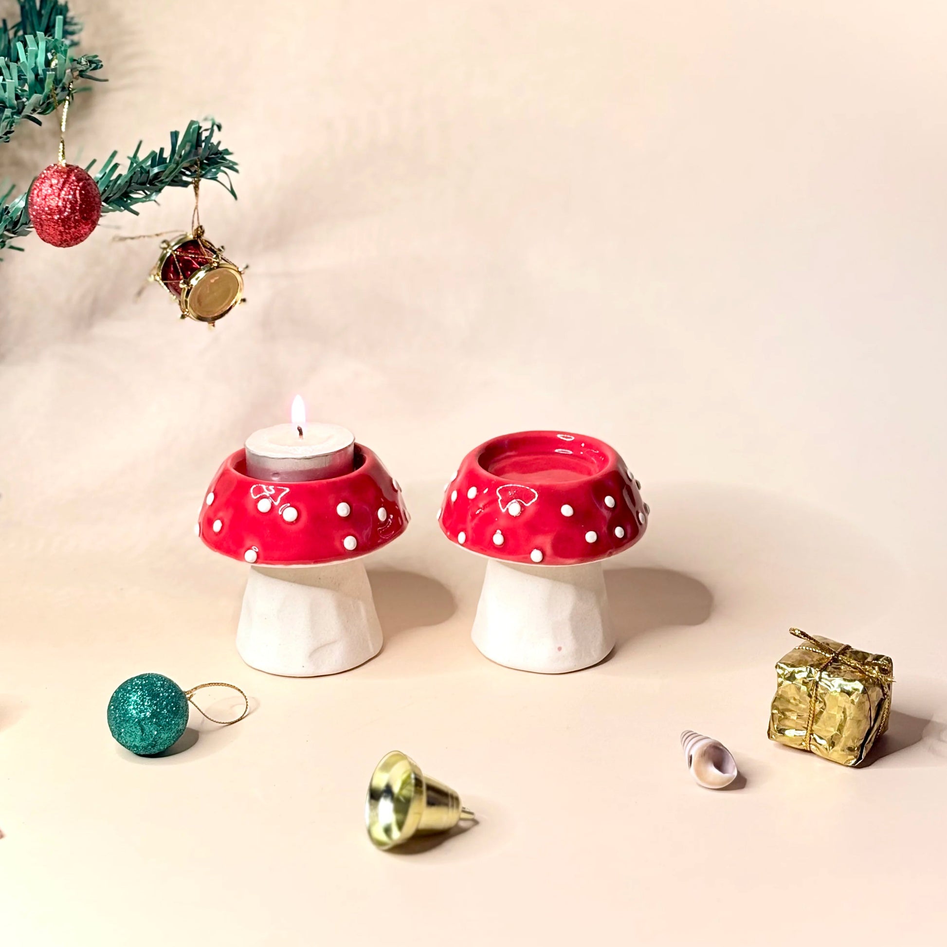 Two red and white polka dot mushroom-shaped candle holders with Christmas decorations on a beige background.