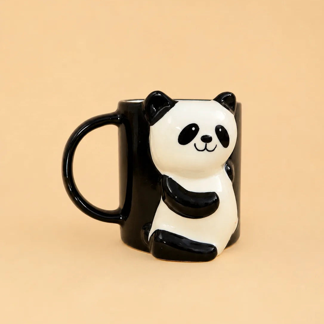 A black ceramic mug shaped like a 3D panda sitting on the side, set against a solid beige background.