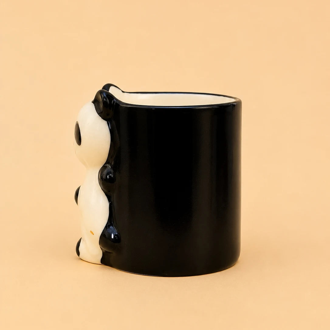 A glossy black ceramic mug with a 3D panda design on the side, set against a solid peach-beige background.