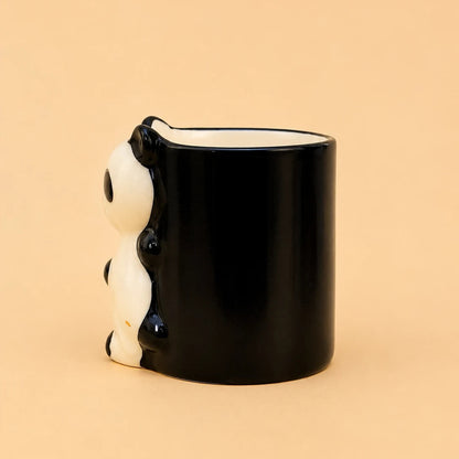 A glossy black ceramic mug with a 3D panda design on the side, set against a solid peach-beige background.