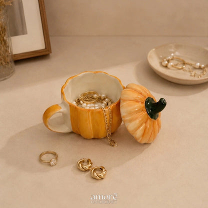 Pumpkin-shaped jewelry box with gold earrings on a beige surface