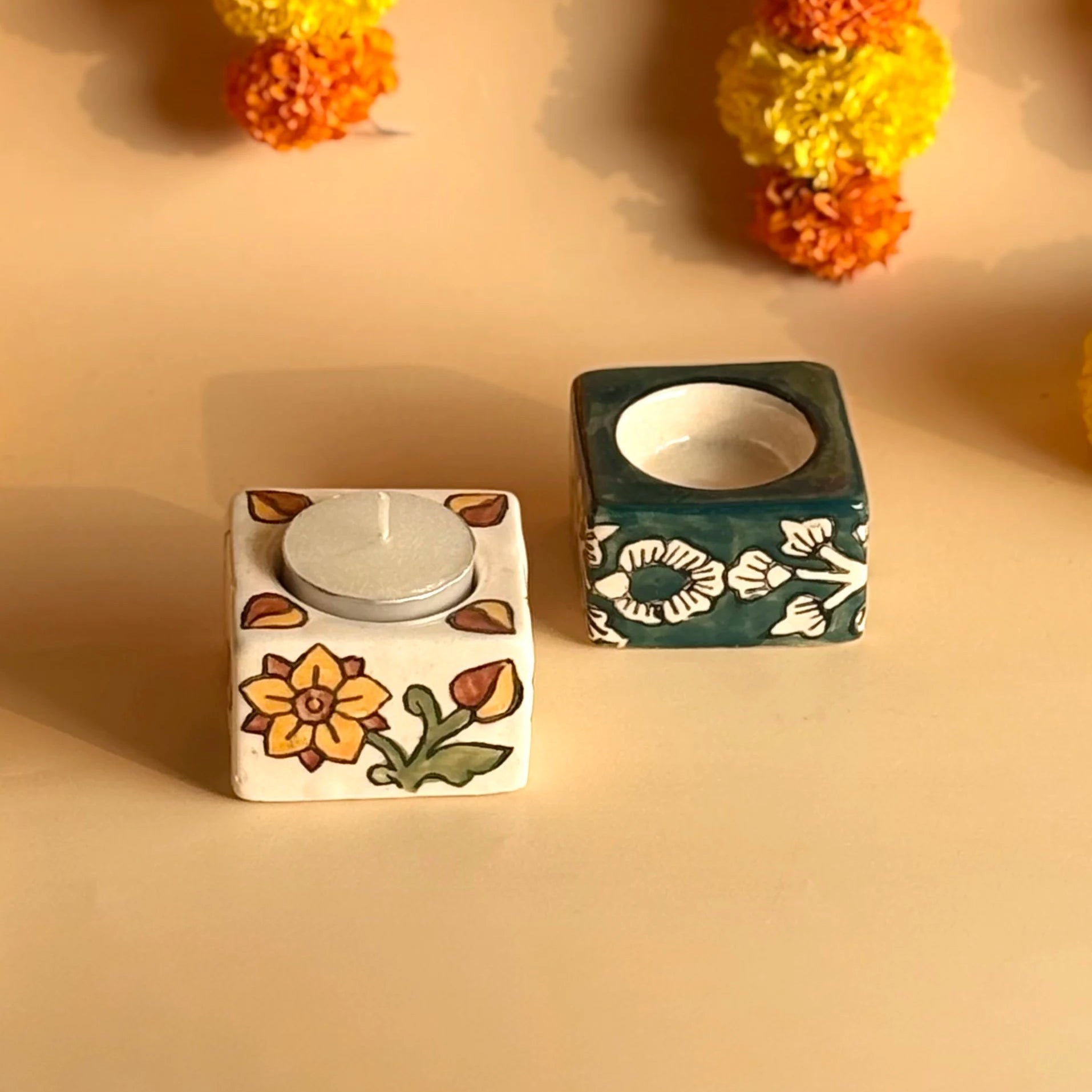 Two square ceramic candle holders with floral designs on a beige background.