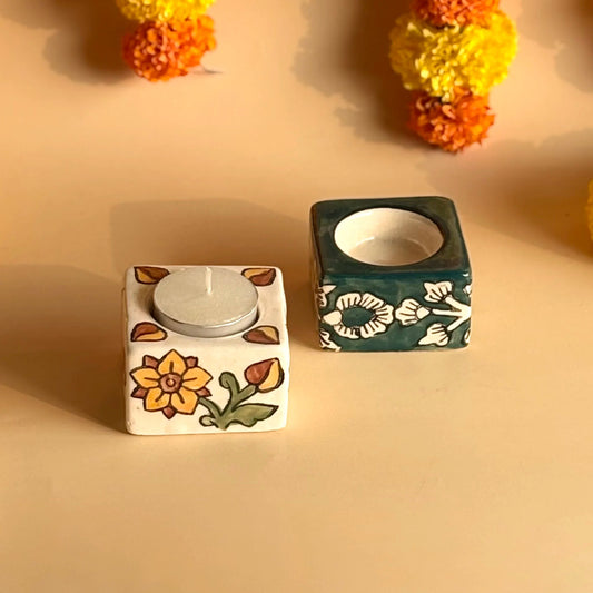 Two square ceramic candle holders with floral designs on a beige background.