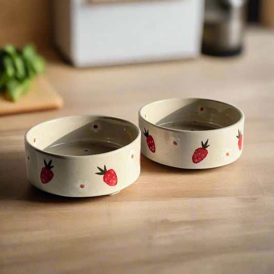 Two ceramic bowls with strawberry designs on a light gray background