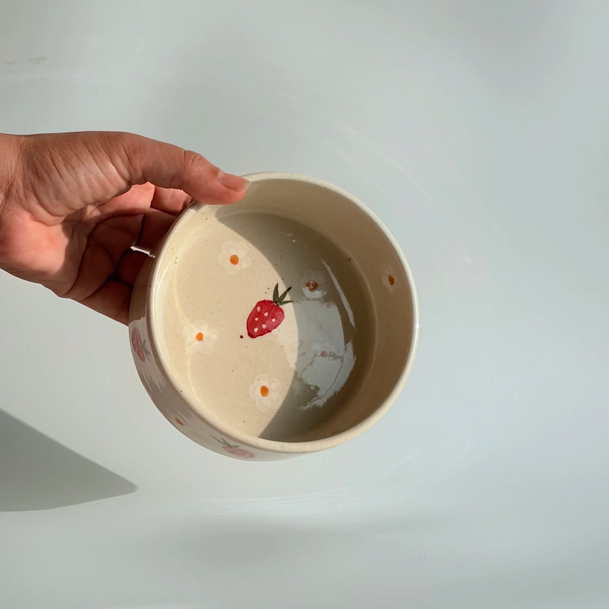 Hand holding a small ceramic bowl with a strawberry design on a plain background