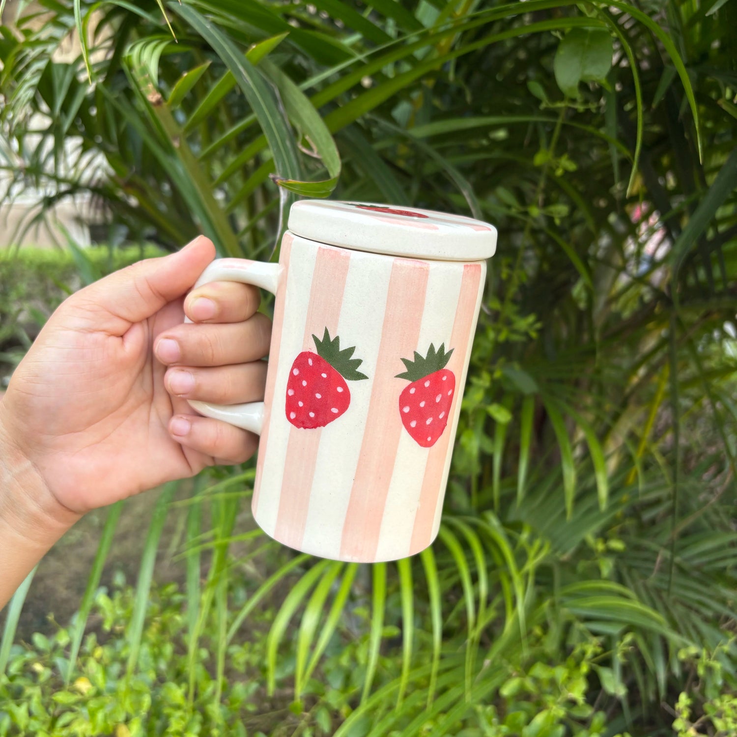 Person holding a mug with strawberry design against a green leafy background